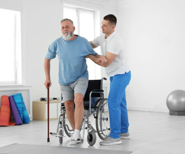 Man in rolstoel bij fysiotherapeut, man probeert te lopen