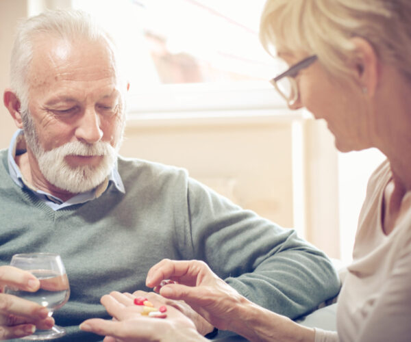 Vrouw helpt oudere man met het uitzoeken van zijn pillen