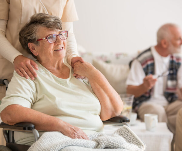 oude dame in rolstoel houdt hand van verpleegster vast