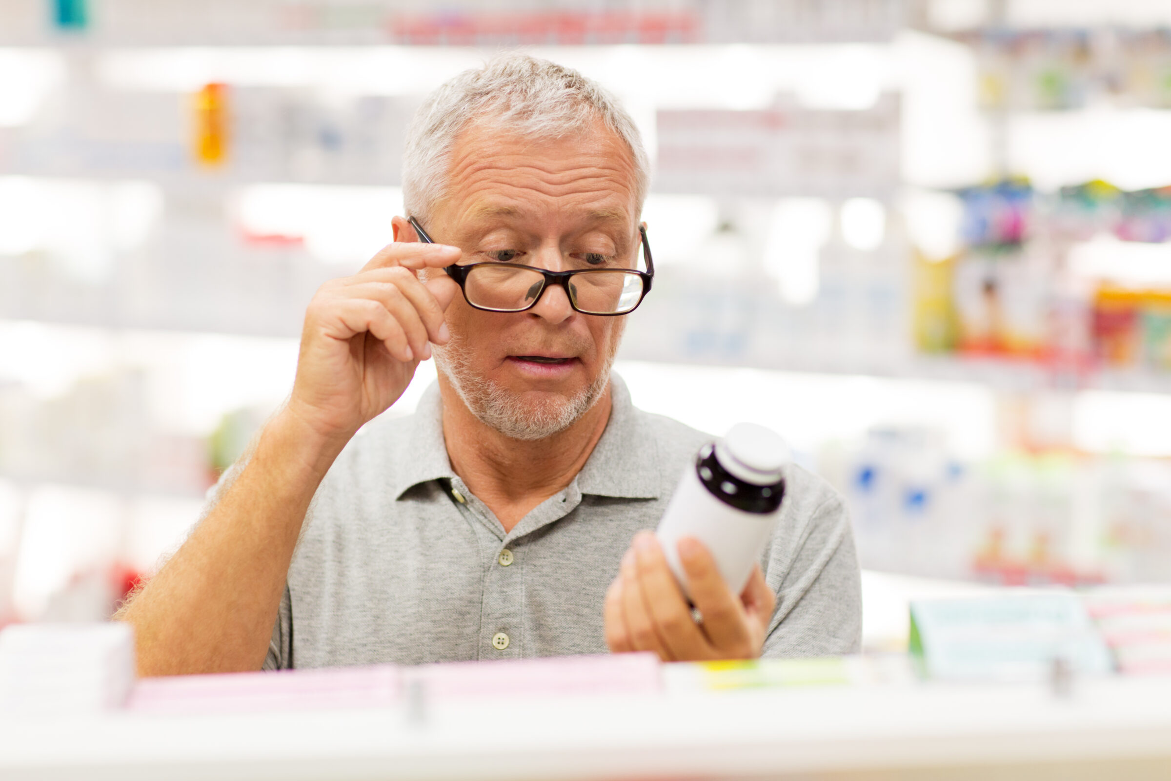 Man met leesbril in de apotheek leest verpakking van pot pillen